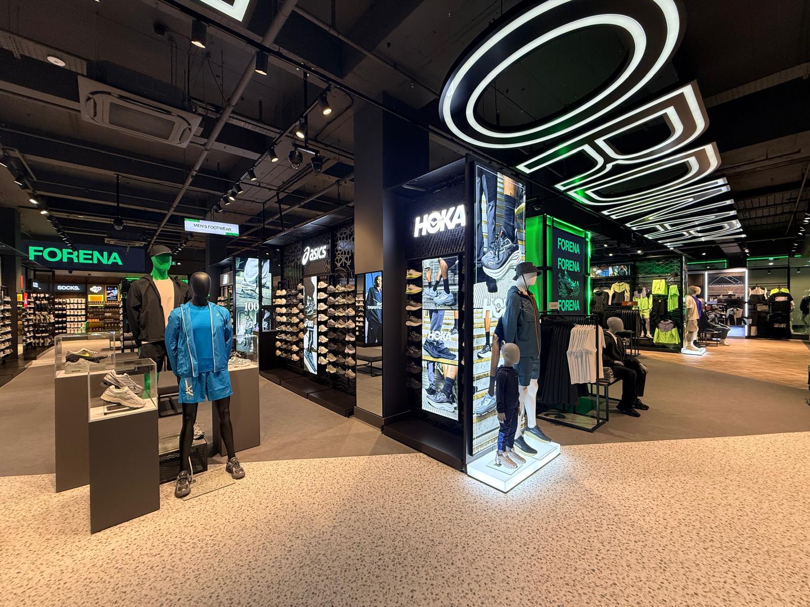 From 130% Turnover to Retail Employer of the Year: How Footasylum Rewired Frontline Comms With Zipline 1 Shoe and athletic apparel store interior with bright lighting, display shelves of sneakers, mannequins in sportswear, and illuminated brand signs including Hoka and Forena.