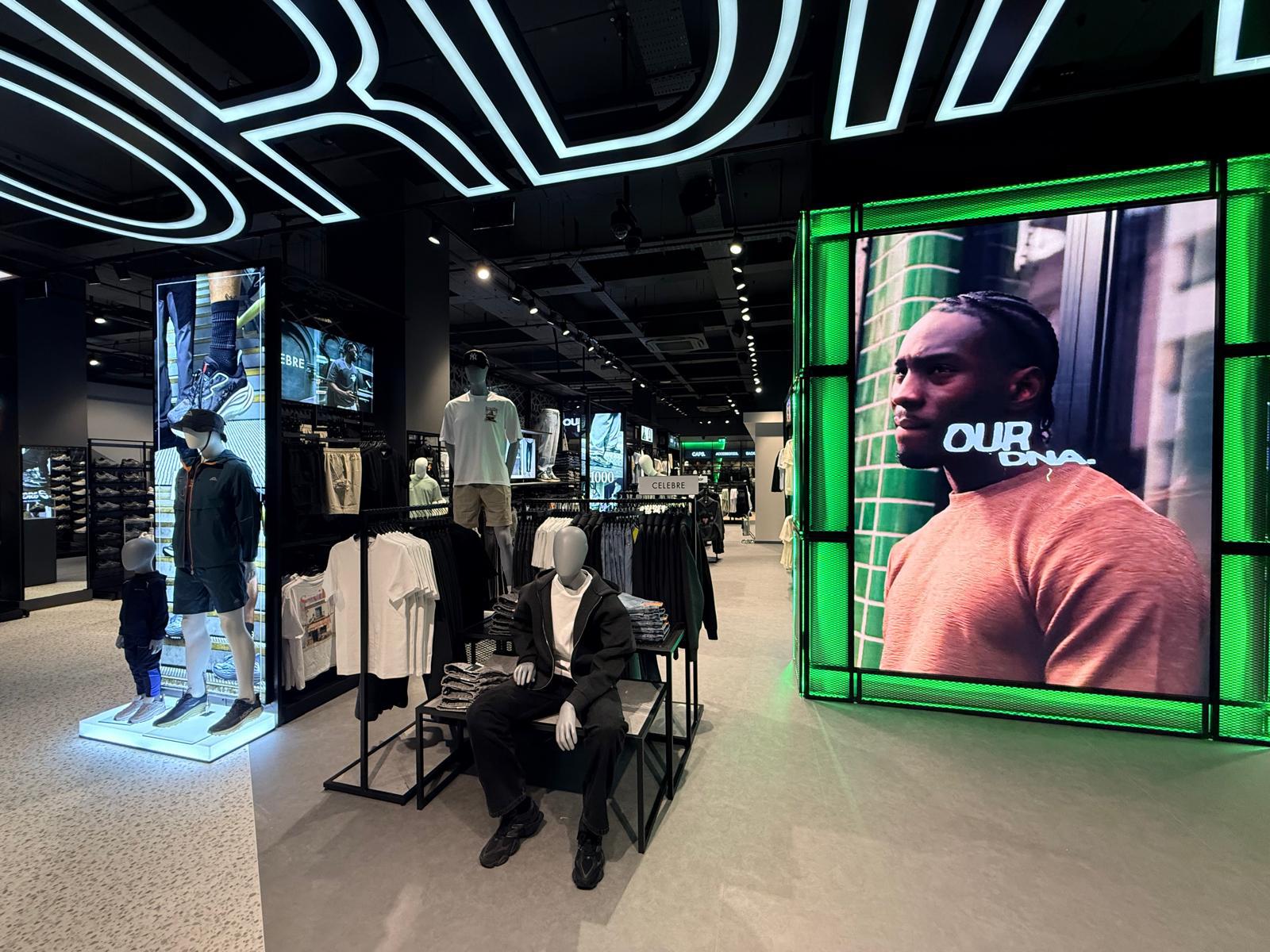 From 130% Turnover to Retail Employer of the Year: How Footasylum Rewired Frontline Comms With Zipline 2 Clothing store interior with mannequins dressed in casual wear and a large digital screen displaying a man in an orange shirt.