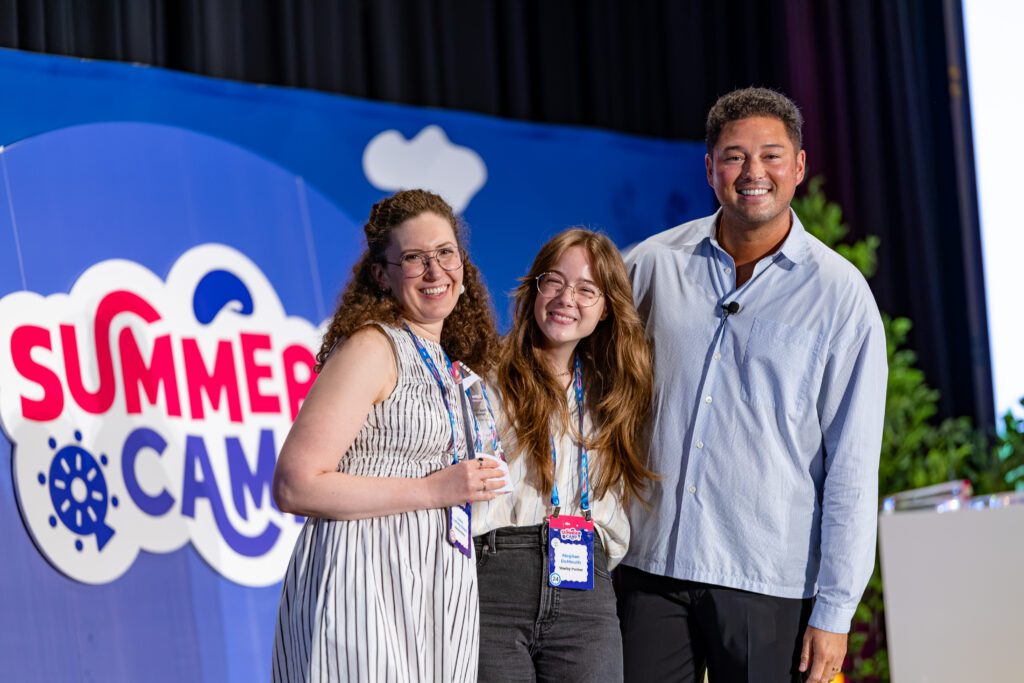 Take a Bow: Celebrating Zipline’s 2026 Summer Camp Award Winners 4 Three people stand smiling together on stage at a summer camp event, with one person holding a trophy. A colorful "Summer Camp" sign is visible in the background.